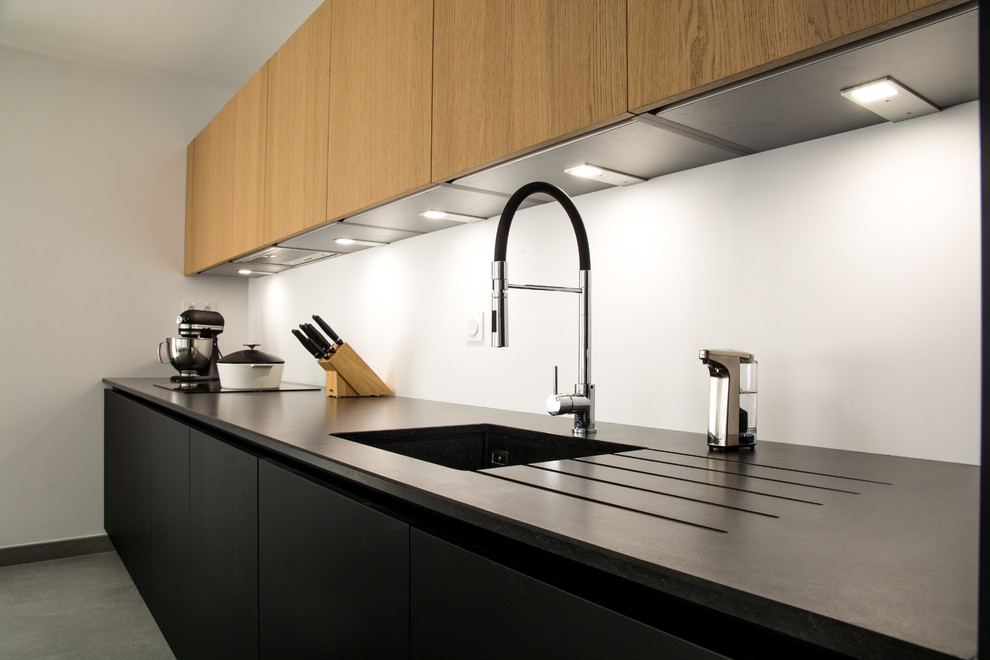 Photo of a medium sized contemporary single-wall open plan kitchen in Grenoble with a submerged sink, flat-panel cabinets, light wood cabinets, granite worktops, black appliances, ceramic flooring, no island, grey floors and black worktops.