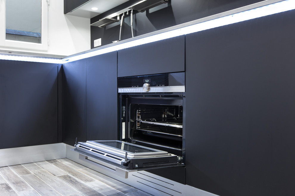 Small modern l-shaped open plan kitchen in Paris with a submerged sink, flat-panel cabinets, black cabinets, black splashback, black appliances, light hardwood flooring and no island.
