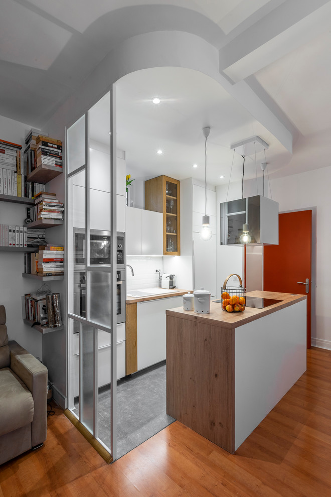 Small modern galley open plan kitchen in Paris with a single-bowl sink, white cabinets, soapstone worktops, white splashback, metro tiled splashback, integrated appliances, ceramic flooring, an island, grey floors and brown worktops.