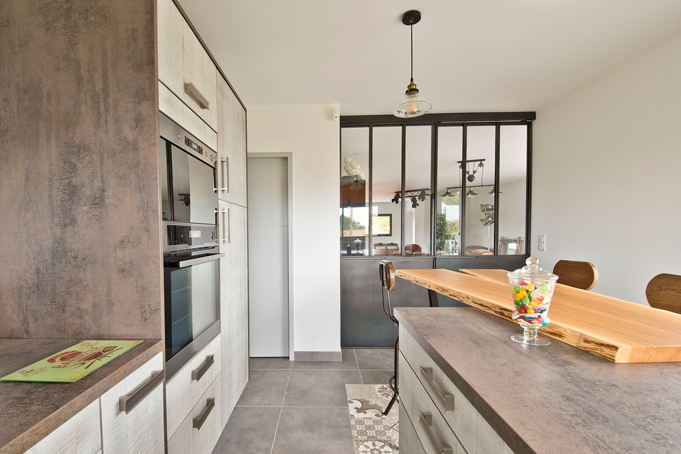 Photo of a large industrial kitchen/diner in Nantes with a built-in sink, flat-panel cabinets, light wood cabinets, laminate countertops, grey splashback, metal splashback, integrated appliances, ceramic flooring, an island and beige floors.