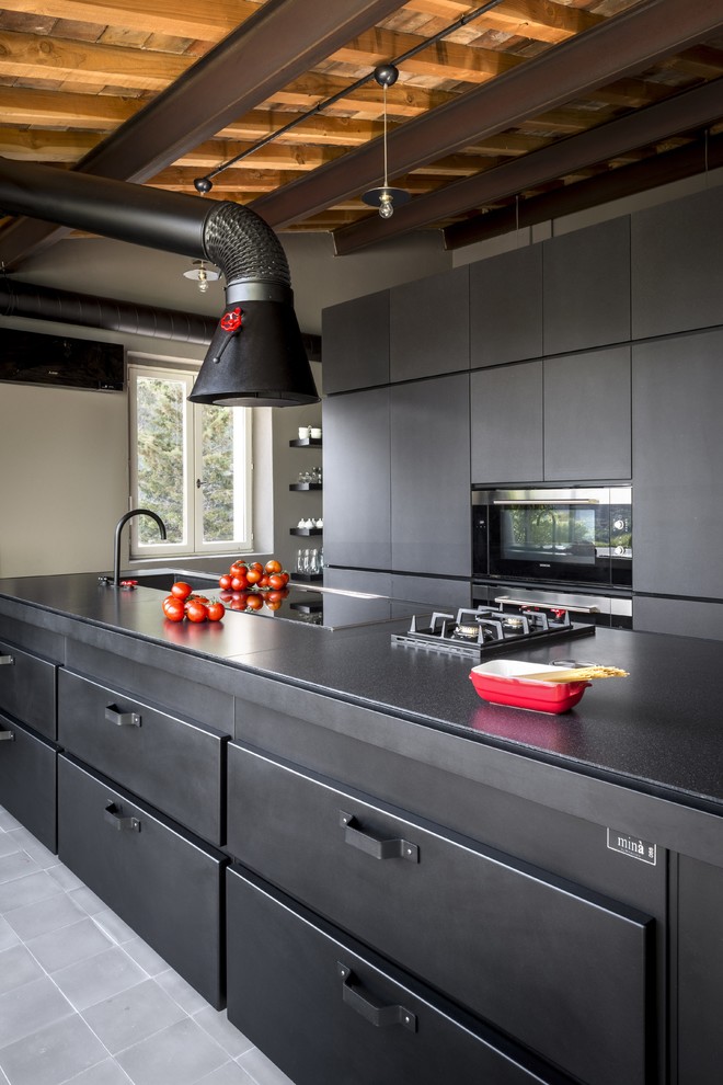 Modelo de cocina industrial abierta con salpicadero negro, electrodomésticos negros, suelo de azulejos de cemento, una isla y suelo gris