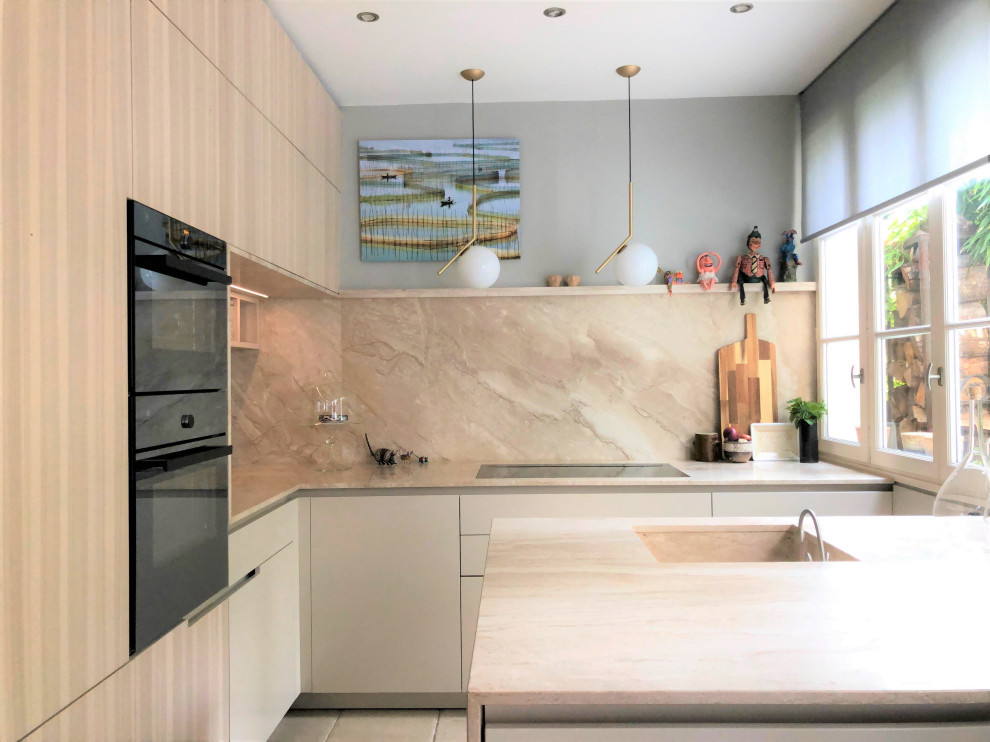 Foto på ett stort funkis beige l-kök, med en enkel diskho, beige skåp, marmorbänkskiva, beige stänkskydd, stänkskydd i marmor, svarta vitvaror, släta luckor, en halv köksö och beiget golv