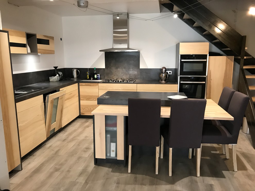 Large contemporary l-shaped open plan kitchen in Other with a single-bowl sink, flat-panel cabinets, light wood cabinets, laminate countertops, grey splashback, black appliances, laminate floors, an island, grey floors and grey worktops.