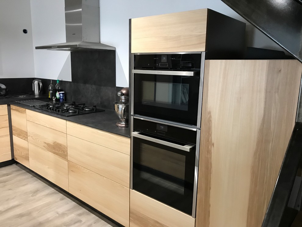 Large contemporary l-shaped open plan kitchen in Other with a single-bowl sink, flat-panel cabinets, light wood cabinets, laminate countertops, grey splashback, black appliances, laminate floors, an island, grey floors and grey worktops.