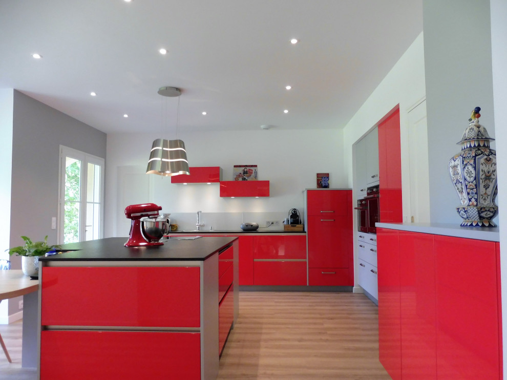 Inspiration for a large modern open plan kitchen in Nantes with a single-bowl sink, flat-panel cabinets, red cabinets, granite worktops, grey splashback, integrated appliances, light hardwood flooring, an island and black worktops.
