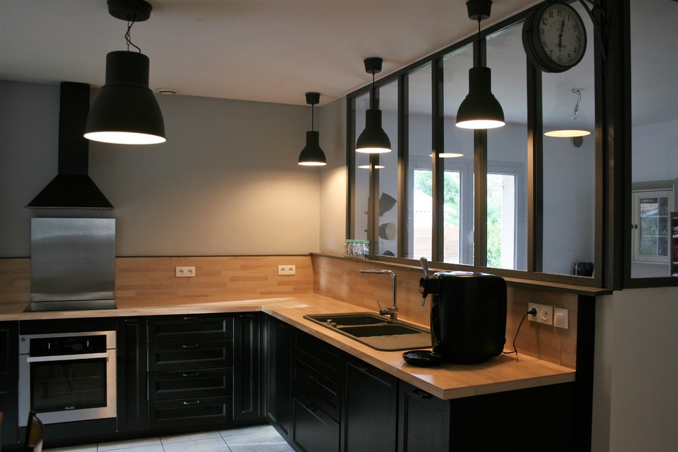 Cette image montre une cuisine ouverte urbaine avec des portes de placard noires, un plan de travail en bois, une crédence noire, une crédence en bois, un électroménager en acier inoxydable, carreaux de ciment au sol et un sol blanc.