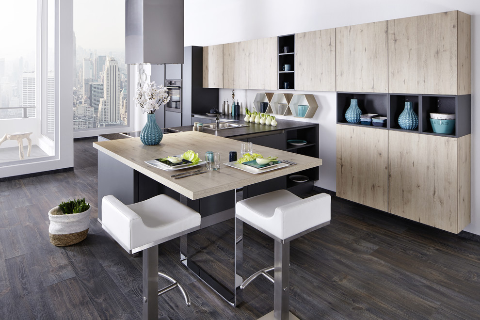 Immagine di una grande cucina minimal con lavello sottopiano, ante lisce, ante in legno chiaro, paraspruzzi grigio, elettrodomestici neri, parquet scuro e pavimento marrone