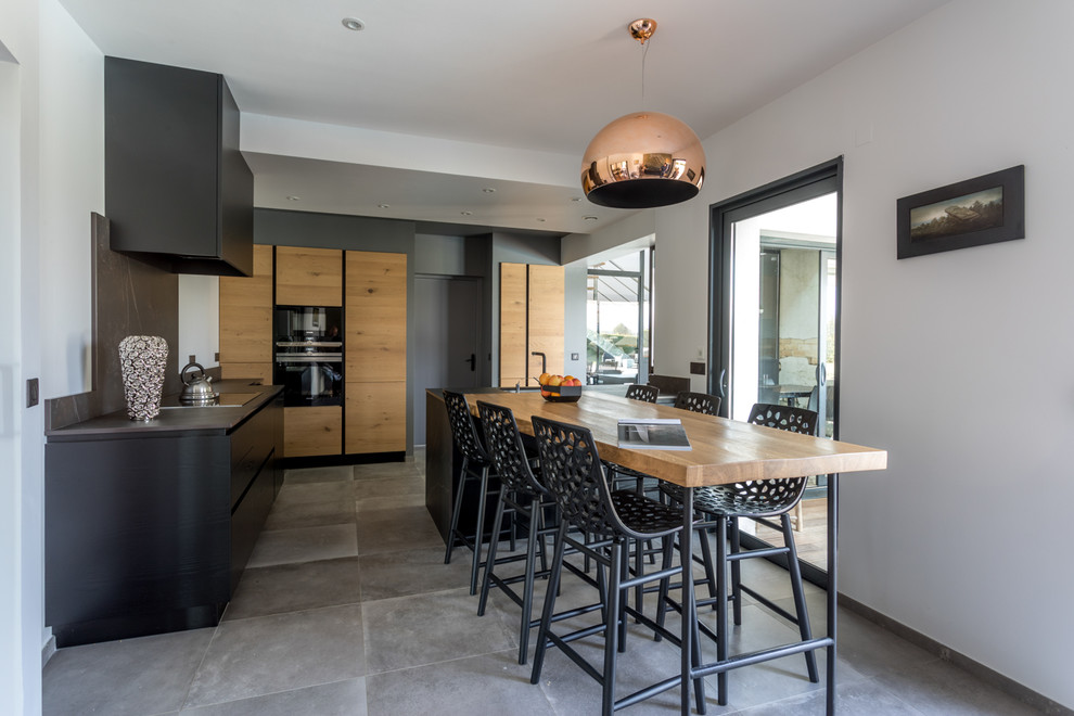 Large contemporary l-shaped open plan kitchen in Bordeaux with an integrated sink, black cabinets, marble worktops, black splashback, stainless steel appliances, cement flooring, an island and grey floors.