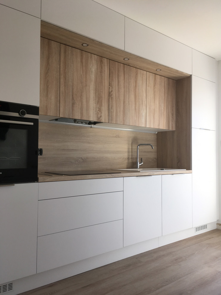 Inspiration for a small modern galley enclosed kitchen in Other with a single-bowl sink, flat-panel cabinets, white cabinets, wood worktops, brown splashback, wood splashback, black appliances, laminate floors, no island, brown floors and brown worktops.