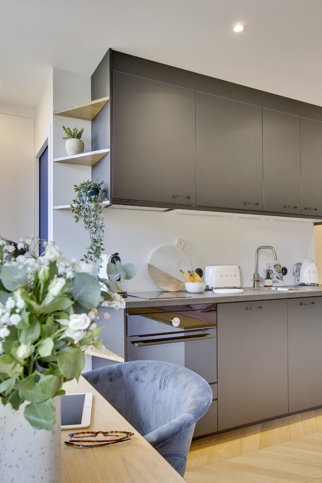 Small eclectic single-wall open plan kitchen in Paris with a submerged sink, beaded cabinets, black cabinets, laminate countertops, white splashback, black appliances, light hardwood flooring, no island, beige floors and grey worktops.