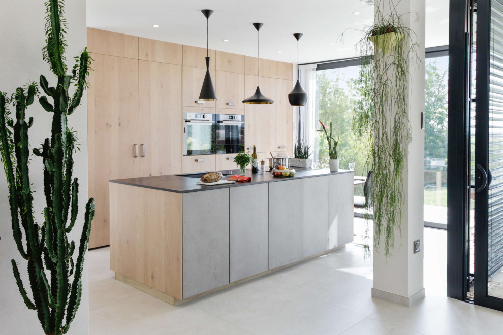 Cette image montre une cuisine parallèle design en bois clair avec un évier encastré, un placard à porte plane, un électroménager en acier inoxydable, îlot, un sol blanc et un plan de travail gris.