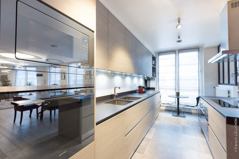 Immagine di una cucina minimalista di medie dimensioni con lavello sottopiano, ante a filo, ante in legno chiaro, paraspruzzi nero, elettrodomestici da incasso e parquet chiaro