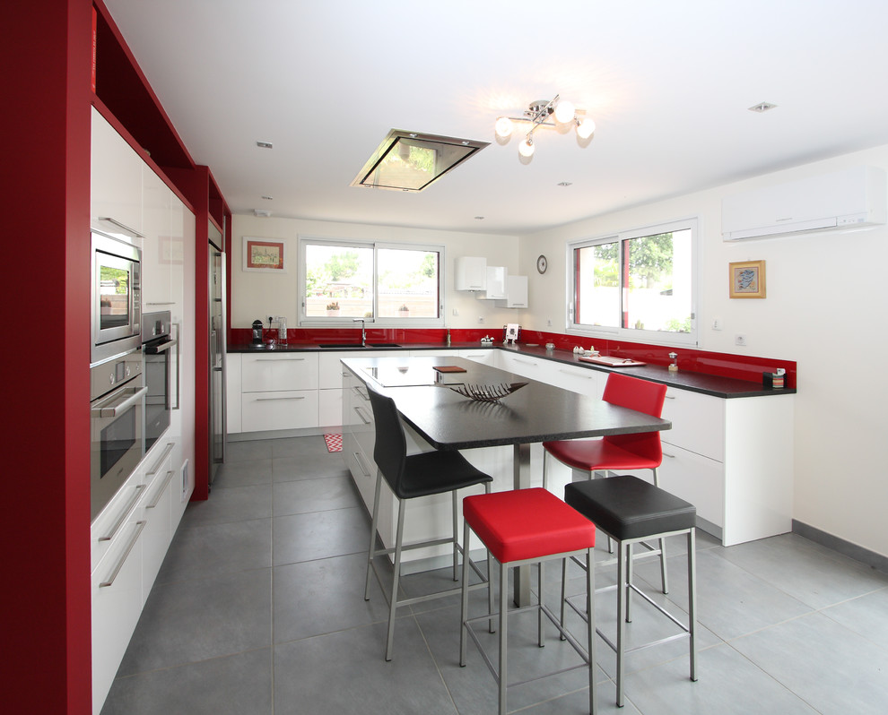 This is an example of a large modern u-shaped open plan kitchen in Angers with an integrated sink, flat-panel cabinets, white cabinets, granite worktops, red splashback, glass sheet splashback, stainless steel appliances, ceramic flooring and an island.