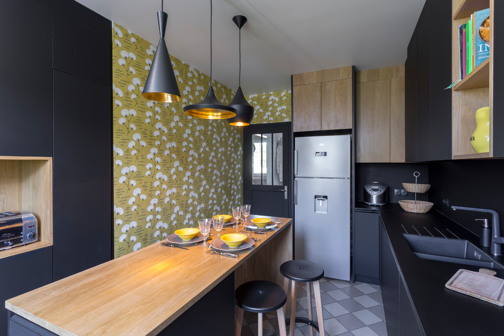 This is an example of a large contemporary enclosed kitchen in Paris with black splashback, stainless steel appliances, an island, grey floors, a double-bowl sink, flat-panel cabinets, black cabinets, wood worktops and beige worktops.