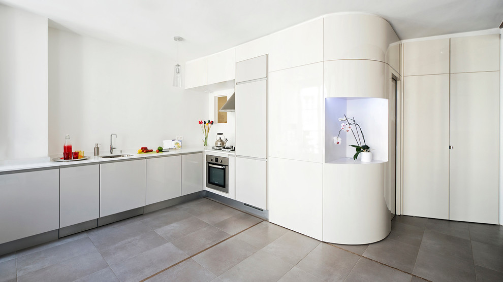 Foto på ett stort, avskilt funkis l-kök, med en undermonterad diskho, släta luckor, vita skåp, vitt stänkskydd, integrerade vitvaror och grått golv