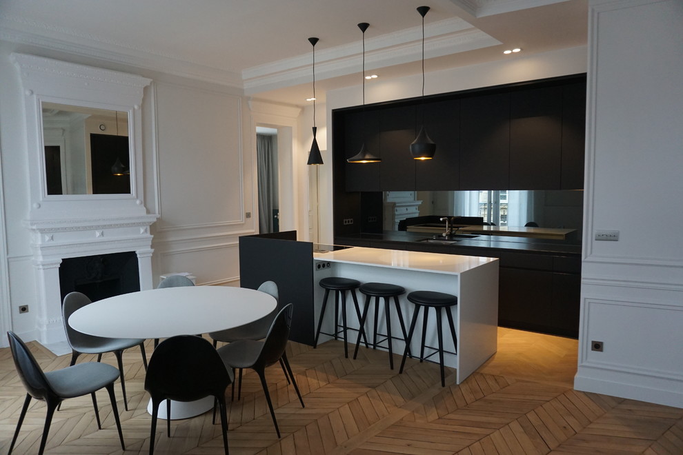 Medium sized contemporary single-wall kitchen/diner in Paris with an island, an integrated sink, flat-panel cabinets, black cabinets, granite worktops, mirror splashback, integrated appliances and light hardwood flooring.