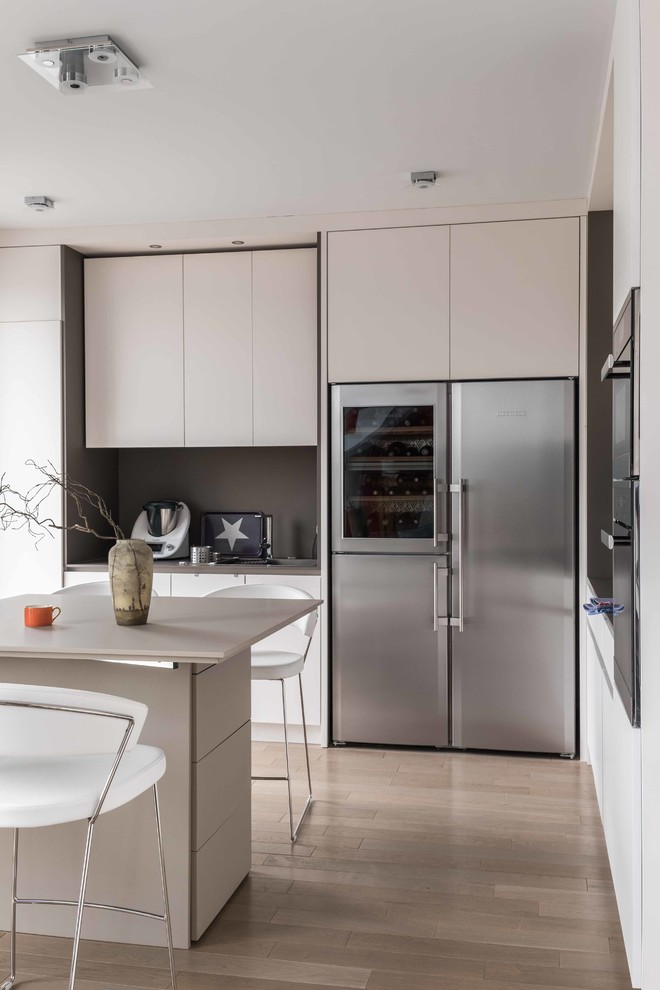Inspiration for a contemporary l-shaped kitchen/diner in Paris with an integrated sink, flat-panel cabinets, white cabinets, wood worktops, grey splashback, wood splashback, stainless steel appliances, light hardwood flooring and an island.