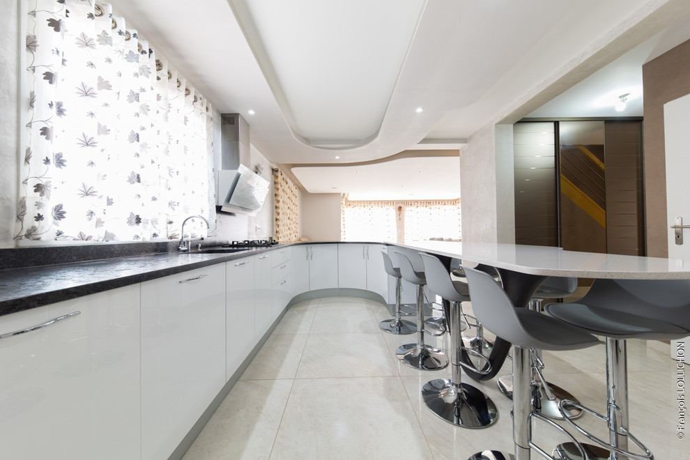 This is an example of a medium sized contemporary u-shaped open plan kitchen in Paris with an integrated sink, recessed-panel cabinets, white cabinets, granite worktops, grey splashback, white appliances, no island and beige floors.