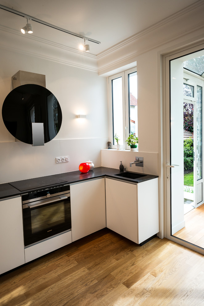 Photo of a medium sized contemporary u-shaped open plan kitchen in Other with a submerged sink, beaded cabinets, white cabinets, granite worktops, white splashback, ceramic splashback, black appliances and no island.