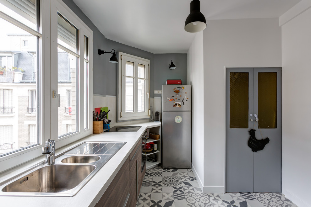 パリにあるお手頃価格の中くらいなコンテンポラリースタイルのおしゃれなキッチン (ダブルシンク、フラットパネル扉のキャビネット、中間色木目調キャビネット、アイランドなし、ラミネートカウンター、白いキッチンパネル、ガラスまたは窓のキッチンパネル、シルバーの調理設備、セメントタイルの床、グレーの床、白いキッチンカウンター) の写真