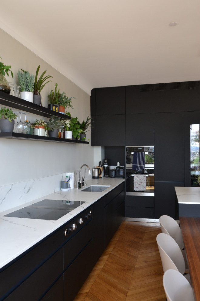 Inspiration for a large contemporary l-shaped open plan kitchen in Paris with a submerged sink, beaded cabinets, black cabinets, engineered stone countertops, white splashback, engineered quartz splashback, stainless steel appliances, light hardwood flooring, an island and white worktops.
