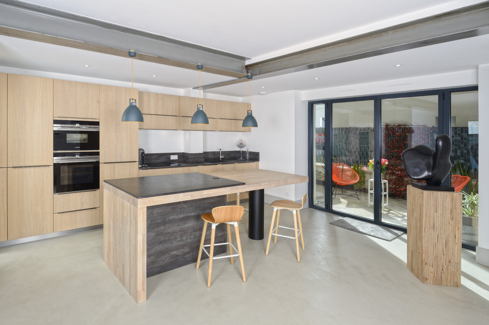 Moderne Küche mit flächenbündigen Schrankfronten, hellen Holzschränken, schwarzen Elektrogeräten, Kücheninsel und beigem Boden in Angers