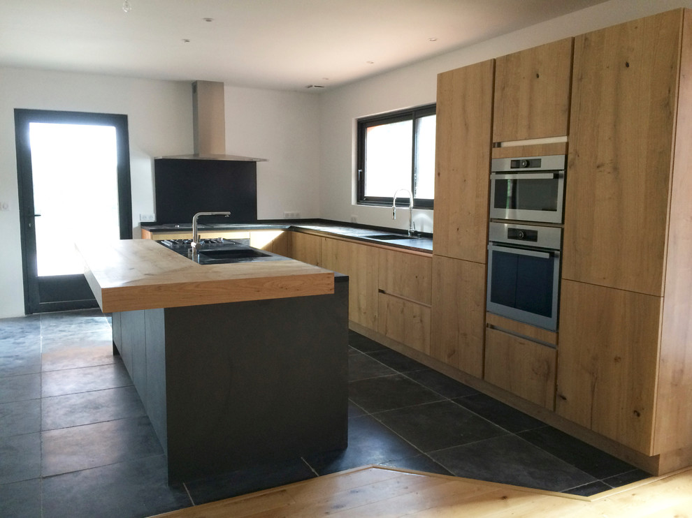 This is an example of a large contemporary l-shaped open plan kitchen in Bordeaux with light wood cabinets, granite worktops, black splashback, stainless steel appliances and an island.