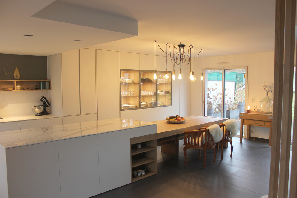 Large scandinavian l-shaped open plan kitchen in Angers with a double-bowl sink, glass-front cabinets, white cabinets, engineered stone countertops, white splashback, mosaic tiled splashback, stainless steel appliances, an island and grey floors.