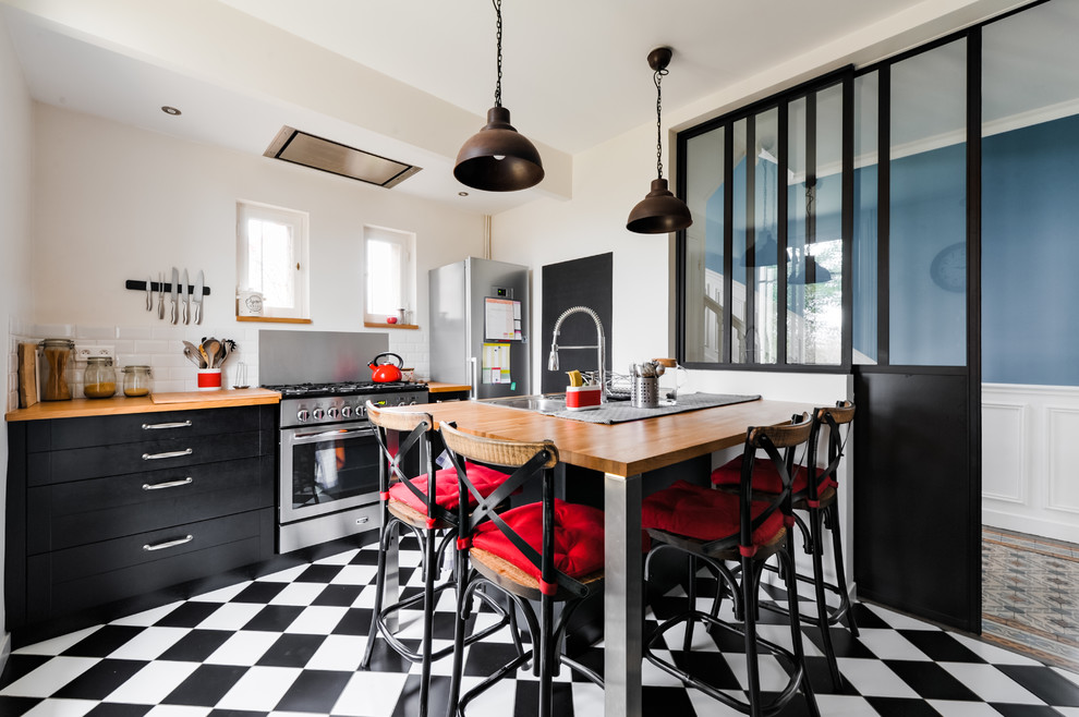 Photo of a medium sized urban galley enclosed kitchen in Paris with a double-bowl sink, shaker cabinets, black cabinets, wood worktops, white splashback, metro tiled splashback, stainless steel appliances, a breakfast bar, ceramic flooring, black floors and brown worktops.