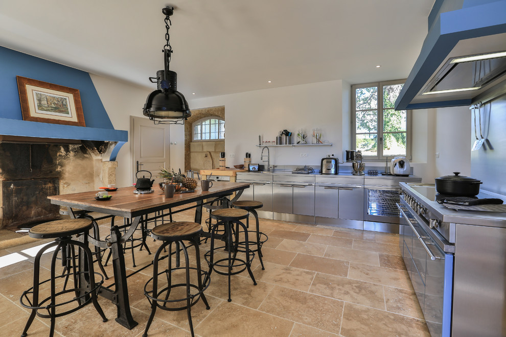 Réalisation d'une grande cuisine américaine champêtre en L et inox avec un placard à porte plane, un plan de travail en inox et un électroménager de couleur.