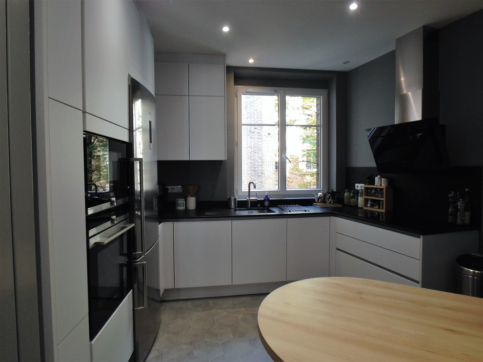 This is an example of a contemporary u-shaped enclosed kitchen in Paris with white cabinets, granite worktops, integrated appliances, cement flooring and grey floors.