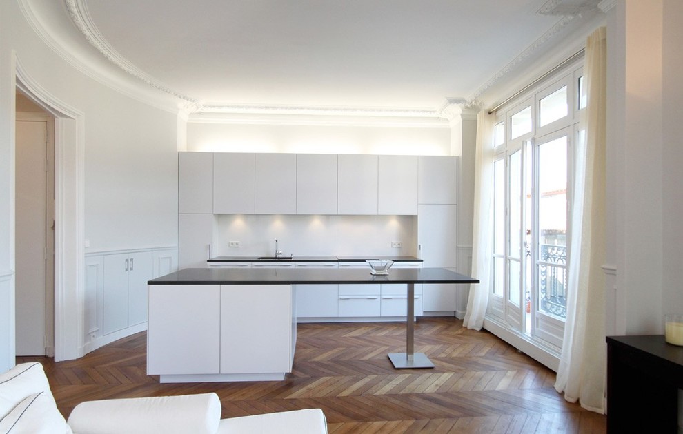Inspiration for a medium sized contemporary galley kitchen/diner in Paris with white cabinets, white splashback, integrated appliances, medium hardwood flooring and an island.