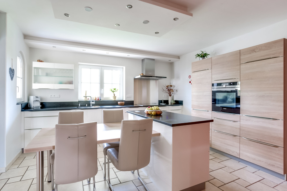 Mittelgroße Moderne Wohnküche in U-Form mit Unterbauwaschbecken, flächenbündigen Schrankfronten, hellen Holzschränken, Küchenrückwand in Schwarz und Kücheninsel in Nancy
