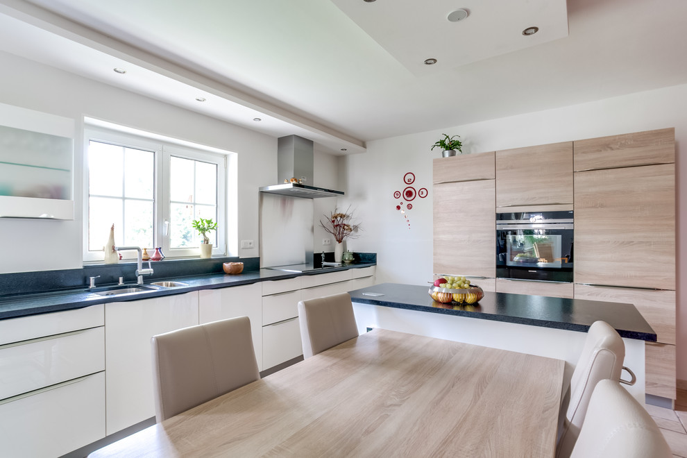 Immagine di una cucina contemporanea di medie dimensioni con lavello sottopiano, ante lisce, ante in legno chiaro e paraspruzzi nero