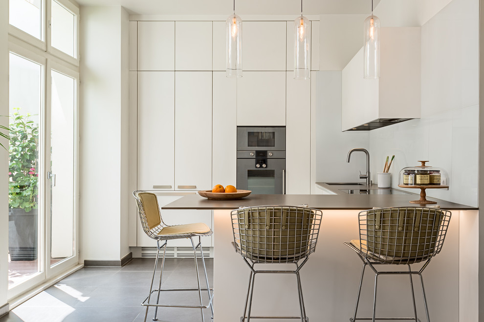 パリにある高級な中くらいなコンテンポラリースタイルのおしゃれなキッチン (シングルシンク、白いキャビネット、白いキッチンパネル、ガラス板のキッチンパネル、シルバーの調理設備、セラミックタイルの床) の写真