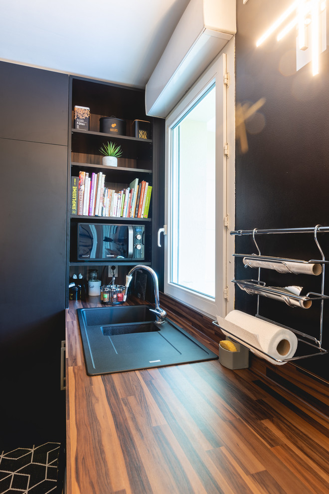 パリにある小さなコンテンポラリースタイルのおしゃれなキッチン (シングルシンク、インセット扉のキャビネット、黒いキャビネット、木材カウンター、黒いキッチンパネル、木材のキッチンパネル、黒い調理設備、淡色無垢フローリング、ベージュの床、ベージュのキッチンカウンター) の写真
