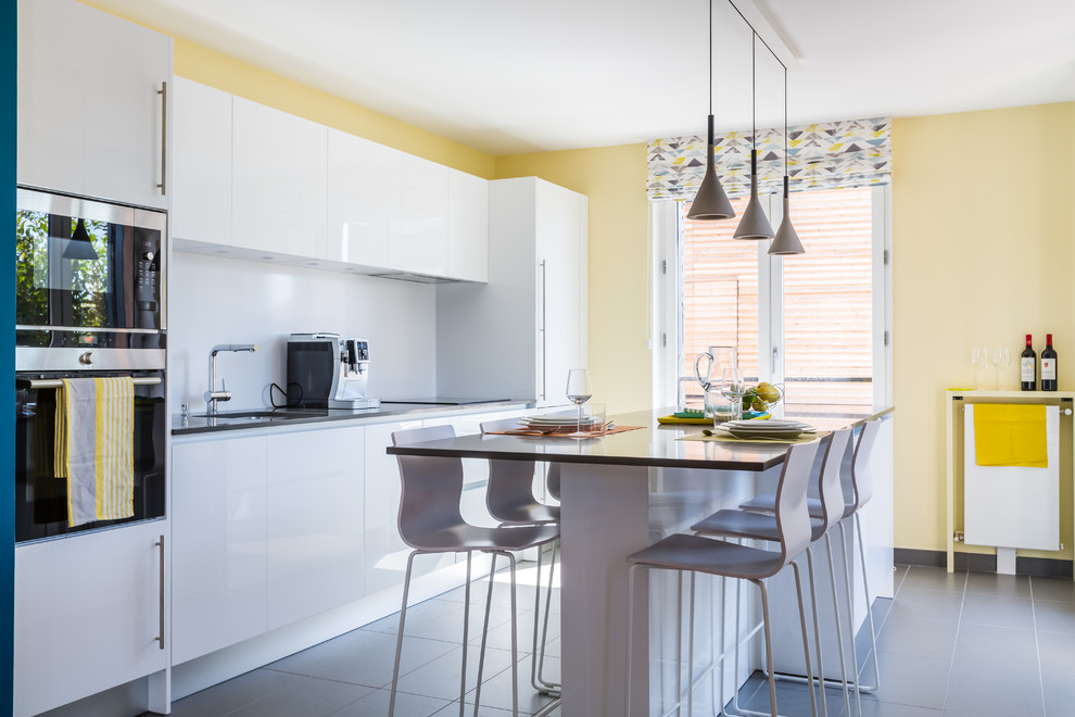 Zweizeilige Moderne Küche mit Unterbauwaschbecken, flächenbündigen Schrankfronten, weißen Schränken, Küchenrückwand in Weiß, Kücheninsel und grauem Boden in Bordeaux