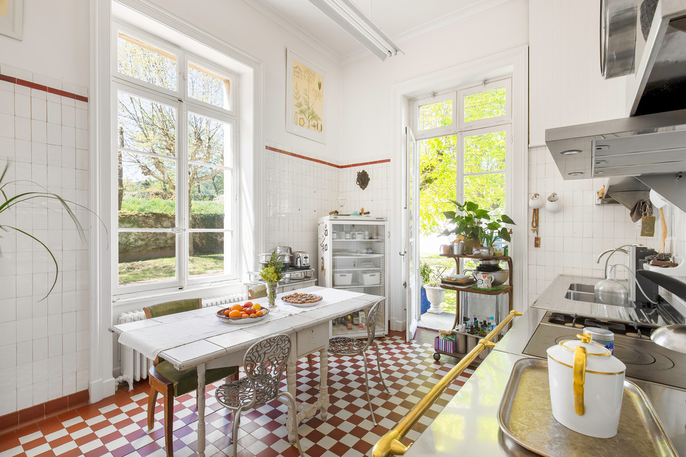 リヨンにあるカントリー風のおしゃれなキッチン (ダブルシンク、ステンレスカウンター、白いキッチンパネル、赤い床、グレーのキッチンカウンター) の写真