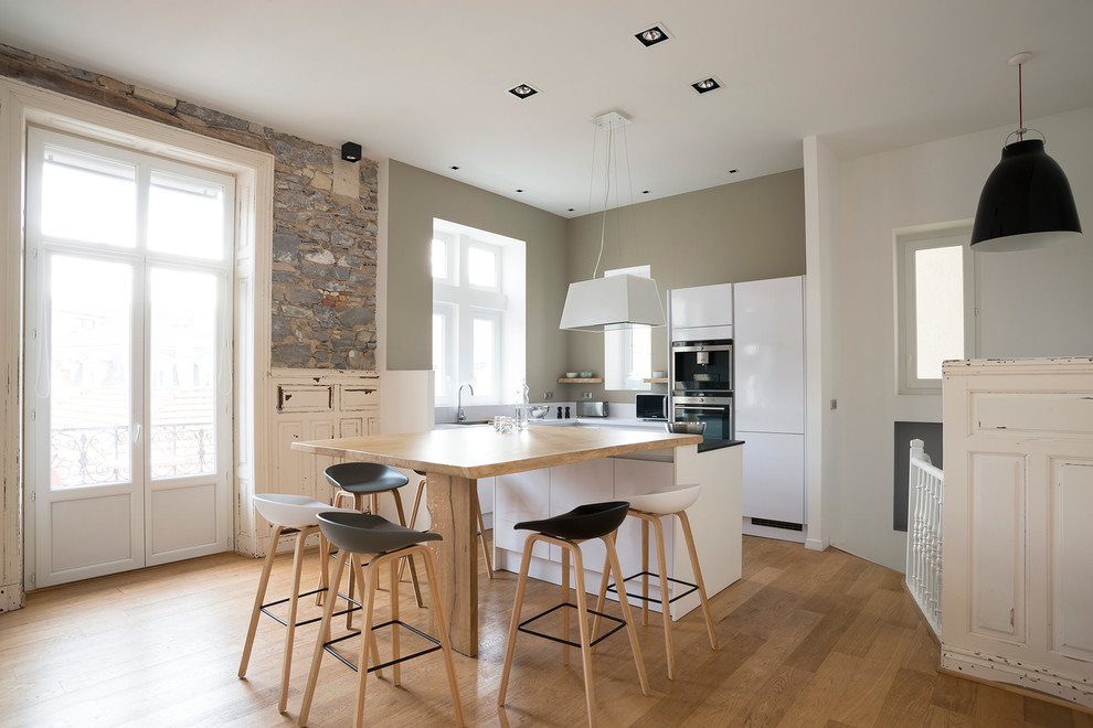 Foto på ett funkis kök, med släta luckor, vita skåp, rostfria vitvaror, ljust trägolv, en köksö och brunt golv