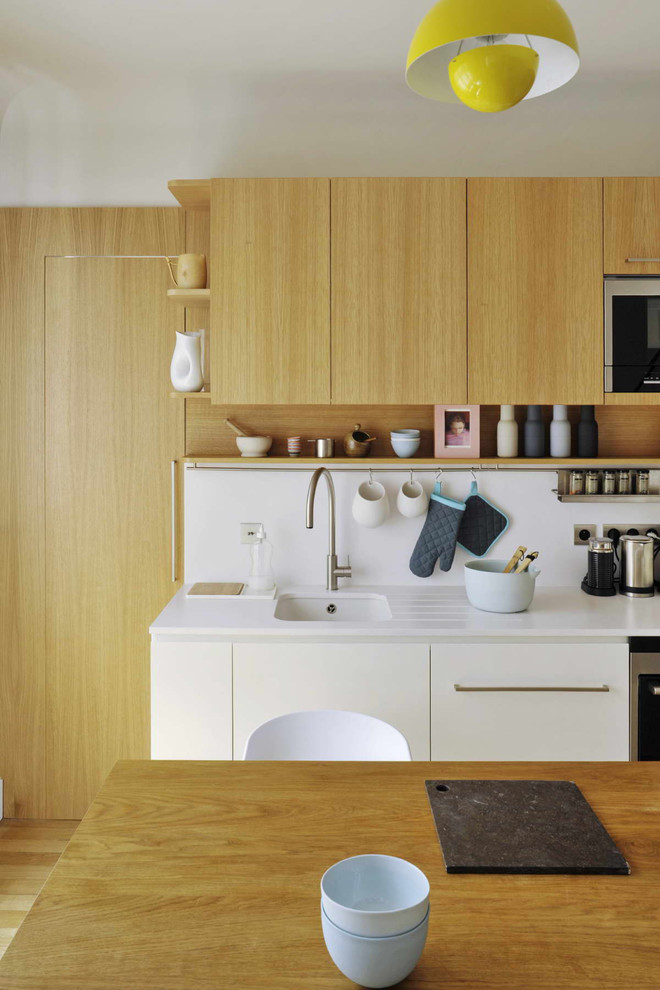 Foto di una cucina minimal di medie dimensioni con lavello sottopiano, ante lisce, ante in legno chiaro, top in superficie solida, paraspruzzi bianco, elettrodomestici da incasso e parquet chiaro