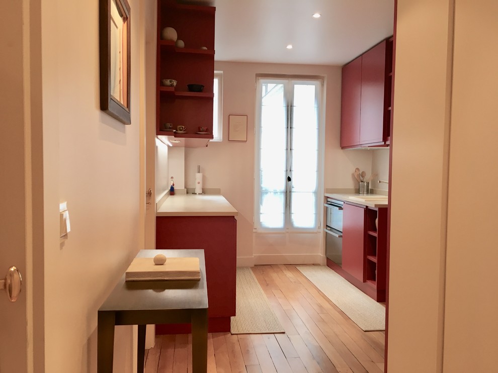 パリにある高級な中くらいなトランジショナルスタイルのおしゃれなキッチン (アンダーカウンターシンク、フラットパネル扉のキャビネット、赤いキャビネット、木材カウンター、ベージュキッチンパネル、石スラブのキッチンパネル、パネルと同色の調理設備、淡色無垢フローリング、茶色い床、ベージュのキッチンカウンター) の写真