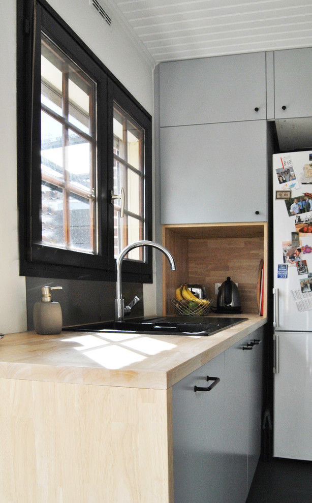 Foto på ett mellanstort minimalistiskt kök, med en undermonterad diskho, släta luckor, träbänkskiva, svart stänkskydd, glaspanel som stänkskydd, svarta vitvaror, klinkergolv i terrakotta, en köksö och grått golv