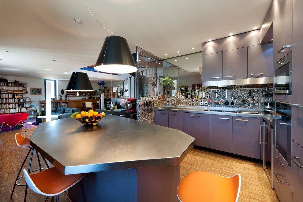 Свежая идея для дизайна: большая угловая кухня-гостиная в современном стиле с серыми фасадами, столешницей из нержавеющей стали и паркетным полом среднего тона без острова - отличное фото интерьера