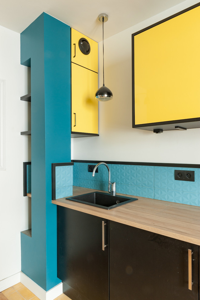 Foto de cocina actual con puertas de armario amarillas, salpicadero azul, suelo de azulejos de cemento y suelo amarillo