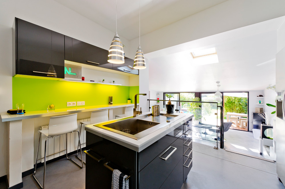 Exempel på ett mellanstort modernt kök, med en enkel diskho, luckor med profilerade fronter, grå skåp, laminatbänkskiva, grönt stänkskydd, rostfria vitvaror, betonggolv och en köksö
