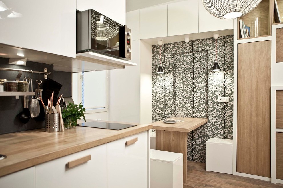 Imagen de cocina comedor lineal contemporánea de tamaño medio sin isla con puertas de armario blancas, salpicadero negro y suelo de madera en tonos medios