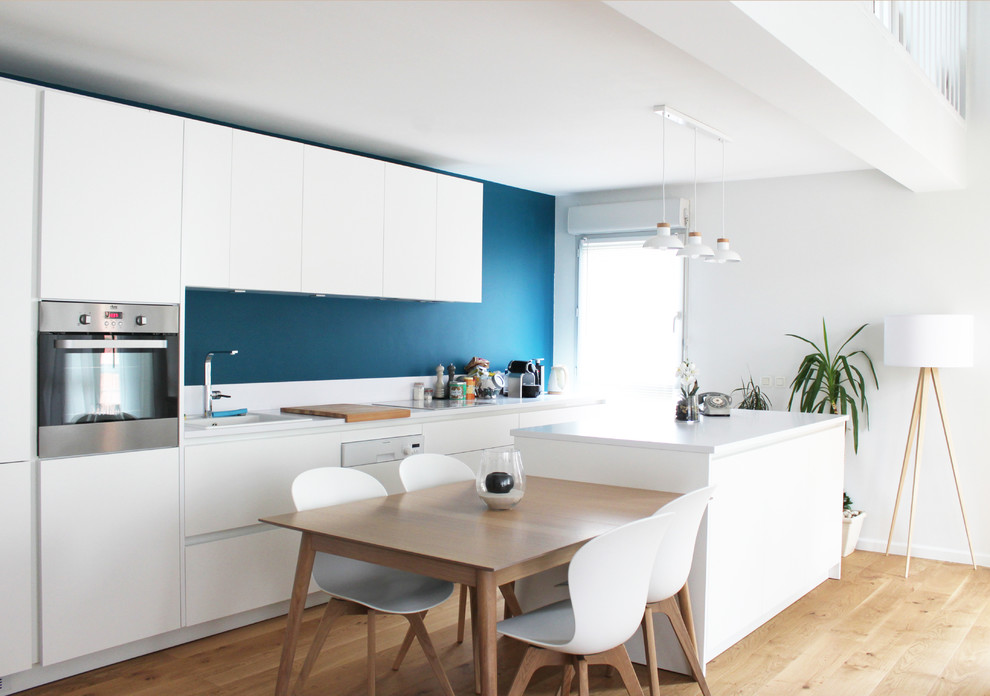 Scandi galley kitchen/diner in Lyon with a built-in sink, flat-panel cabinets, white cabinets, stainless steel appliances, light hardwood flooring and an island.