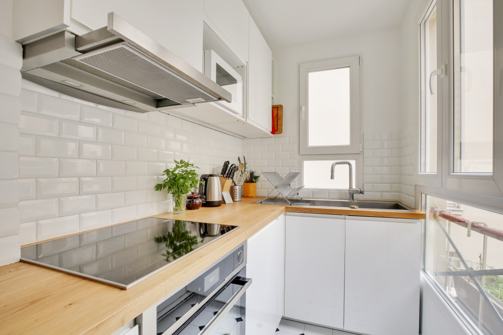 パリにあるラグジュアリーな小さなコンテンポラリースタイルのおしゃれなL型キッチン (ドロップインシンク、フラットパネル扉のキャビネット、白いキャビネット、木材カウンター、白いキッチンパネル、サブウェイタイルのキッチンパネル、シルバーの調理設備、アイランドなし、白い床、茶色いキッチンカウンター) の写真