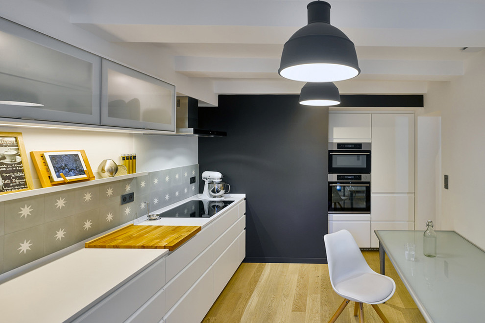 Foto di una cucina lineare design chiusa con ante bianche, paraspruzzi grigio, top bianco, paraspruzzi con piastrelle di cemento, parquet chiaro e pavimento beige