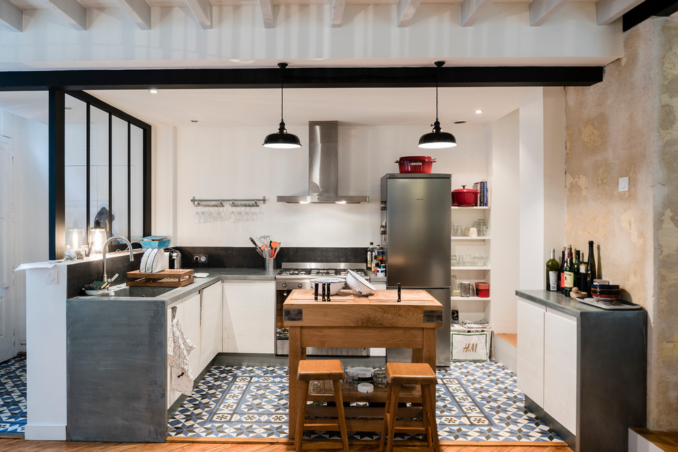 Foto på ett mellanstort industriellt kök, med bänkskiva i zink, svart stänkskydd, rostfria vitvaror, klinkergolv i keramik, en undermonterad diskho, vita skåp och en köksö